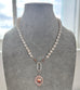 Pearl necklace with a sterling silver 1932 watch fob on a gray mannequin against a window background