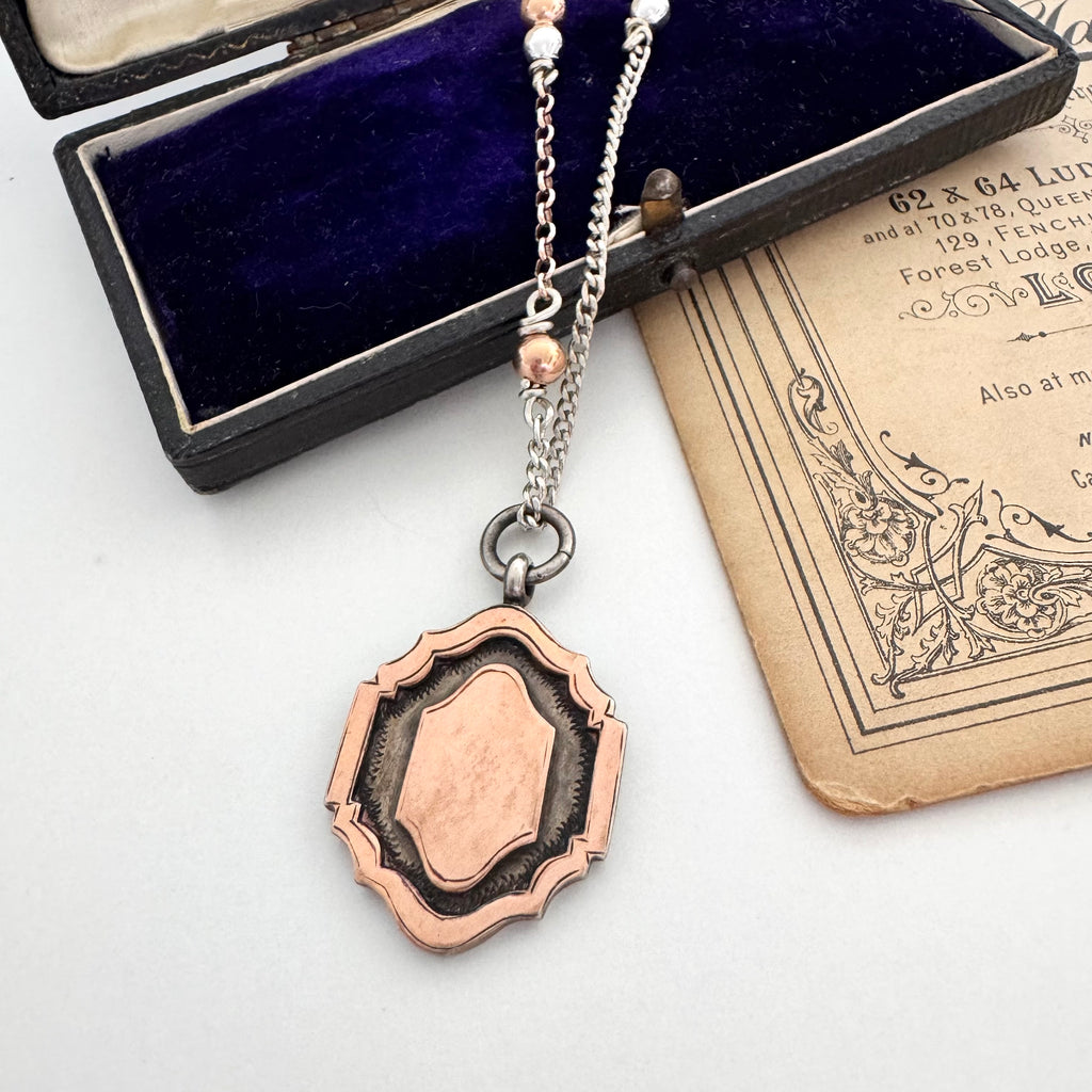 1933 eatch fob necklace with a pendant on a white surface with an old book and jewelry box.