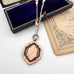 1933 eatch fob necklace with a pendant on a white surface with an old book and jewelry box.