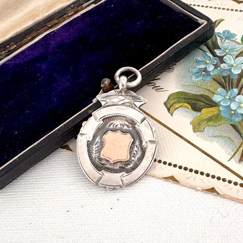 Vintage silver and rose gold watch fob on a floral card with a dark blue box in the background