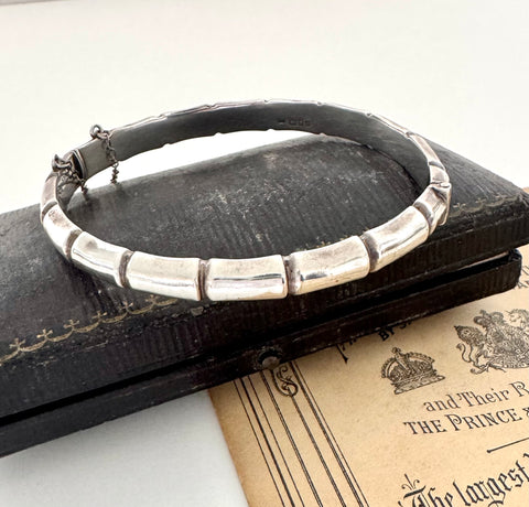 Sterling silver bamboo bangle hallmarked London 1985 sitting on a vintage jewellery box and an antique advertising postcard. 