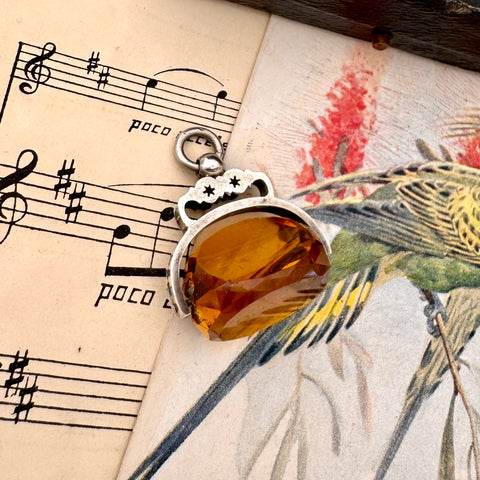 Antique 1891 silver and citrine spinning fob on an old sheet of music with bird illustrations.