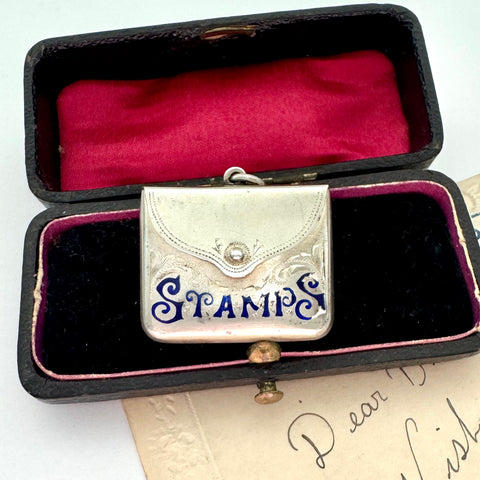 Antique 1911 Crisford & Norris silver stamp case with 'STAMPS' in blue enamel in a black box with red interior.