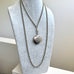 A silver-toned guard chain necklace with a round antique compact locket pendant, displayed on a light gray fabric jewelry bust.