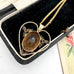 Gold necklace with a heart-shaped pendant featuring a brown stone, displayed in a black jewelry box.
