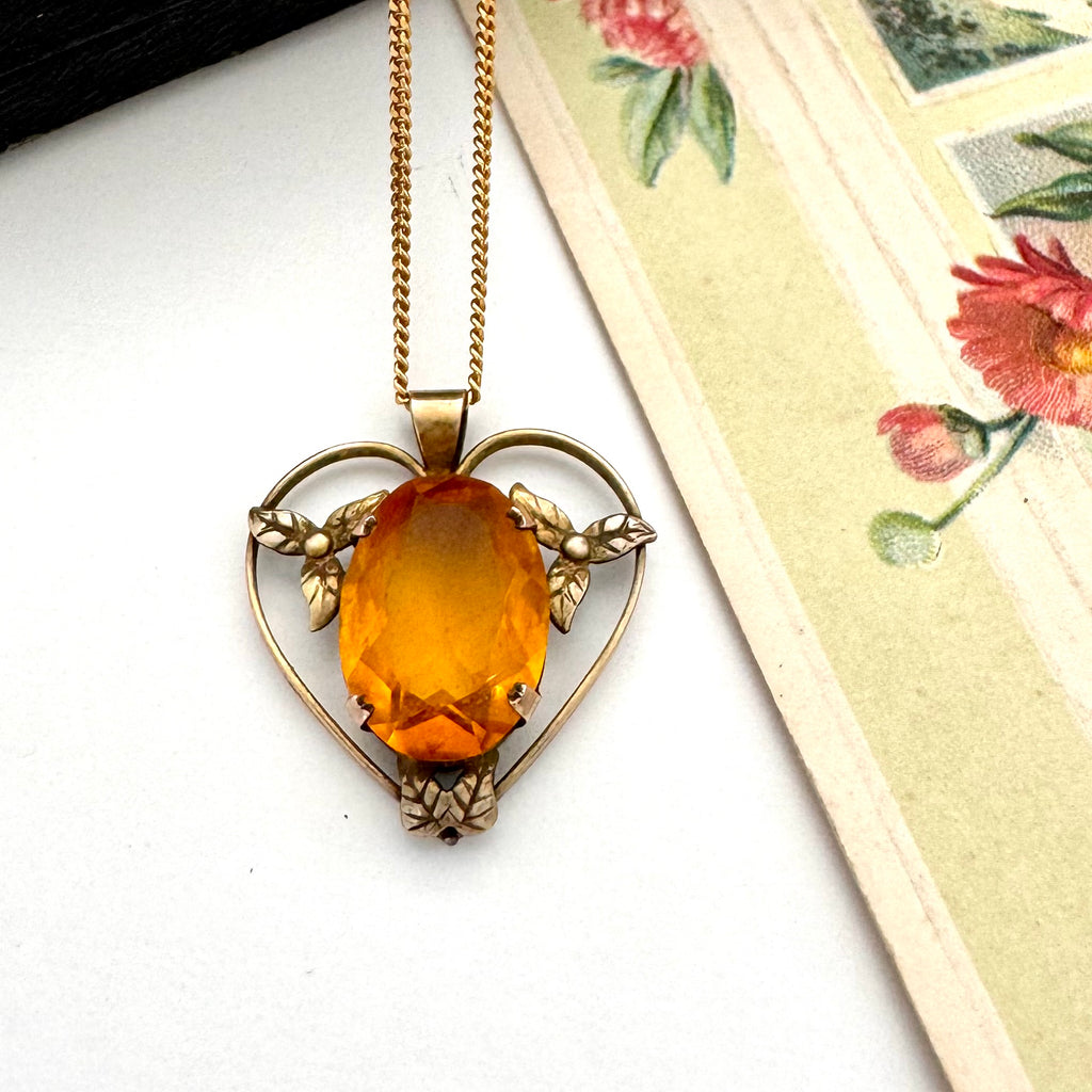 Antique heart-shaped pendant with a yellow gemstone on a chain, placed on a floral card.