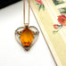 Antique heart-shaped pendant with a yellow gemstone on a chain, placed on a floral card.