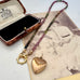 A beaded tourmaline necklace with an antique Etruscan revival 9ct gold lined heart pendant, displayed on a vintage-style card next to an open jewelry box. The beads transition from dark green to pinkish-purple, and the pendant is gold-toned with engraved details. 