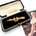 Vintage 9ct gold lined horseshoe and nail brooch with a red gemstone on a white surface with a blurred background