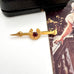 Vintage 9ct gold lined horseshoe and nail brooch with a red gemstone on a white surface with a blurred background