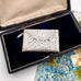 Decorative antique sterling silver stamp case on vintage jewellery box and a floral and vintage-style background