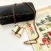 Antique Edwardian stanhope Lourdes binoculars necklace on a chain with a black case and floral illustration in the background.
