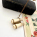 Antique Edwardian stanhope Lourdes binoculars necklace on a chain with a black case and floral illustration in the background.