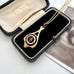 A gold pendant necklace with a circular design and a small pink gemstone, displayed inside an open vintage black velvet jewelry box.