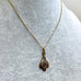 A gold chain necklace with a teardrop-shaped pendant featuring a central circular design with a red center, displayed on a textured light gray mannequin bust.