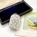 Antique sterling silver 1887 vesta case with intricate patterns on a white surface next to an open jewelry box and vintage card.