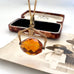 An antique Victorian paste citrine spinning fob necklace, displayed on a vintage-style printed card next to a wooden jewelry box.