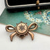 Antique Victorian star burst and bow-shaped brooch  displayed on a white surface with a floral card and a black box in the background.