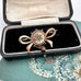Antique Victorian star burst and bow-shaped brooch  displayed on a vintage jewellery box and with a floral card in the background.