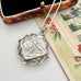 A silver pendant necklace with an ornate filigree border and a square floral engraving, resting on a vintage floral card next to an open antique-style jewelry box.
