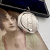 Antique silver compact locket on a white surface with an old photograph of a woman in the background.