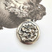 Sterling silver art nouveau repousse floral locket on a white background with an engraved cherub design in the background.