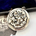 Sterling silver art nouveau repousse floral locket on a white background with an engraved cherub design in the background.