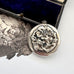 Sterling silver art nouveau repousse floral locket on a white background with an engraved cherub design in the background.