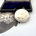 Back of sterling silver art nouveau repousse floral locket on a white background with an engraved cherub design in the background.