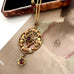  Antique Edwardian art nouveau lavalier  necklace with a geometric openwork design and a small dangling flower charm, both set with dark red gemstones, displayed on a vintage illustrated card.