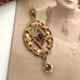 Antique Edwardian art nouveau lavalier  necklace with filigree detailing, featuring a central purple gemstone and a dangling flower-shaped red gemstone, displayed against a vintage sepia-toned portrait background.