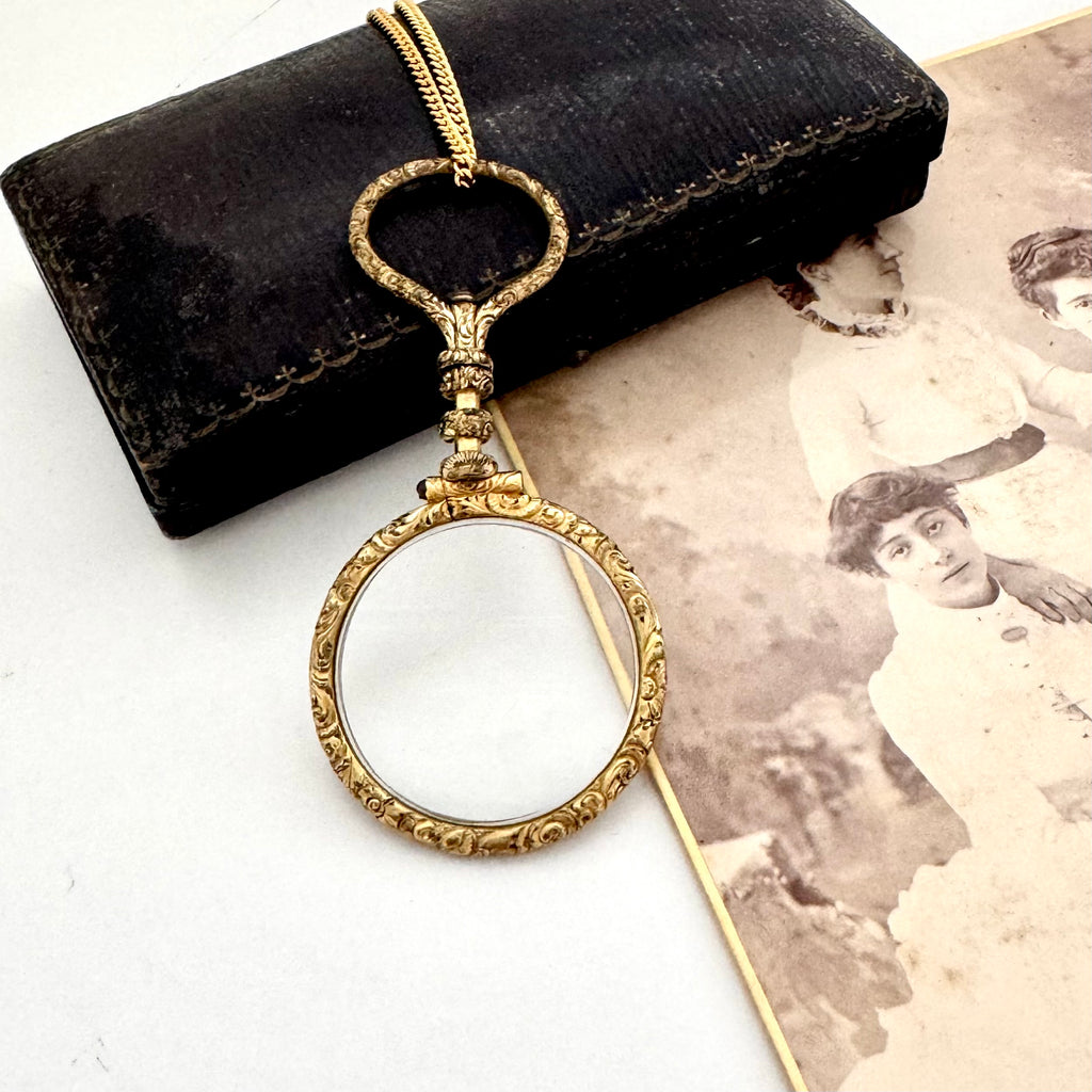 Antique gold magnifying glass necklace on a white surface with an old photograph
