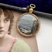 Antique rolled gold pendant with scenic design on a surface next to an old photograph