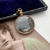 Antique rolled gold pendant with scenic design on a surface with an old photograph