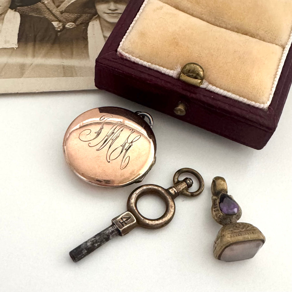 Vintage pocket watch, key, and pendant on a white surface with an open jewelry box.