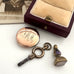 Vintage pocket watch, key, and pendant on a white surface with an open jewelry box.