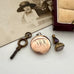 Vintage key, locket with initials, and fob on a white surface with an old photograph in the background.