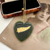 Antique pounamu nephrite jade heart pendant necklace with a gold fern leaf and NZ detail, displayed on a vintage photograph next to an open jewelry box.