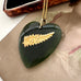 Antique 9ct gold and pounamu green jade heart pendant necklace with a gold fern leaf and the letters 'NZ' engraved on the front, resting on a beige surface.