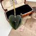 An antique heart-shaped dark green jade pounamu and 9ct gold pendant necklace with a gold chain, displayed inside an open vintage wooden jewelry box with a black velvet lining.