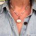 Necklace with a round pendant worn by a person wearing a denim shirt.