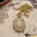 An antique oval locket pendant necklace with an ornate floral engraving, resting on a vintage sepia-toned photograph of a woman. The locket is attached to a gold-tone chain with a lobster clasp.