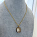 A gold chain necklace with an oval, textured pendant displayed on a gray velvet jewelry bust.