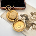 An antique gold-toned sovereign case is shown open, resting on top of an old sepia photograph. A rectangular wooden keepsake box with a black velvet interior is visible in the upper left against a plain light background.