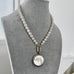Pearl necklace with a pendant on a gray mannequin bust.