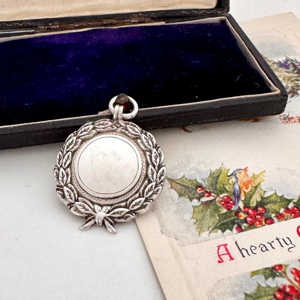 Antique silver watch fob in an open jewelry box with a Christmas-themed card underneath
