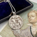Antique silver pendant necklace on a gray surface with an old book and illustration in the background. The pendant features Cupid and Psyche in relief and has been converted from an antique button.
