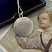 Antique silver pendant necklace on a gray surface with an old book and illustration in the background. 