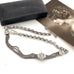 Silver chain with tassels on a white surface next to a black wallet and vintage photo.