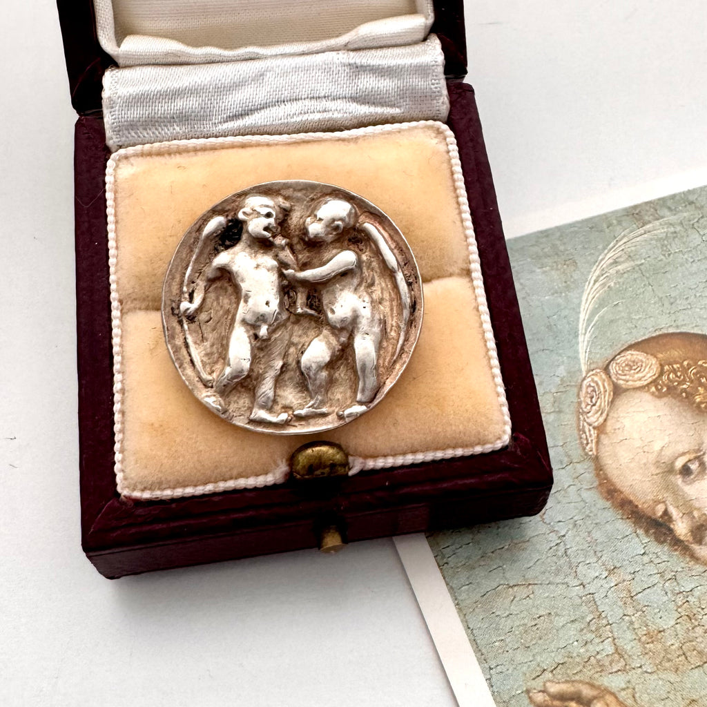 Antique silver button with relief sculpture in a wooden box on a white surface.